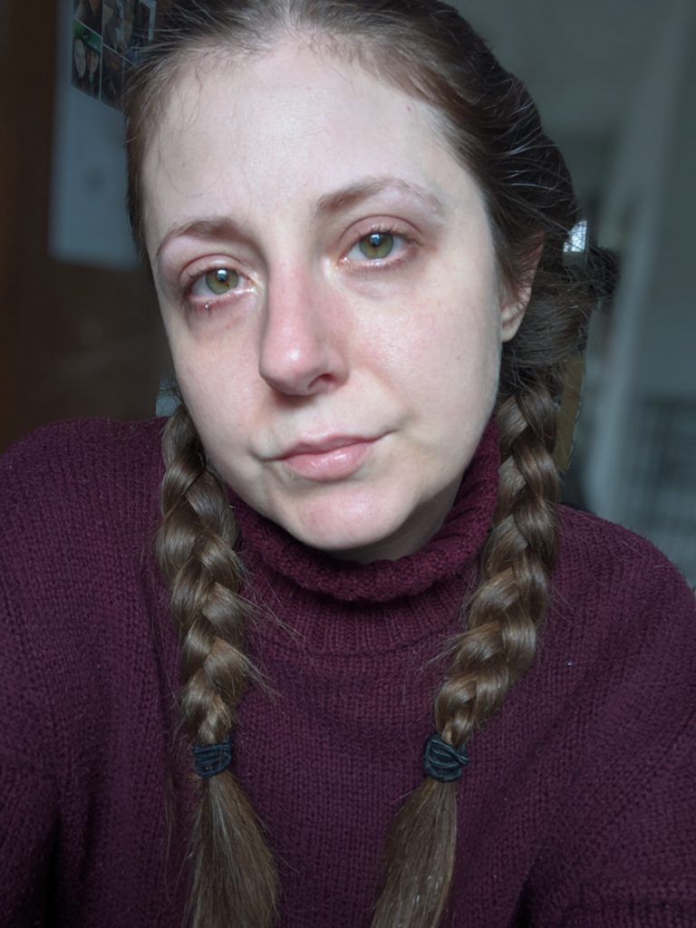 Brianna McInerny wearing a burgundy turtle neck with her hair in braids, with tears in her red eyes.
