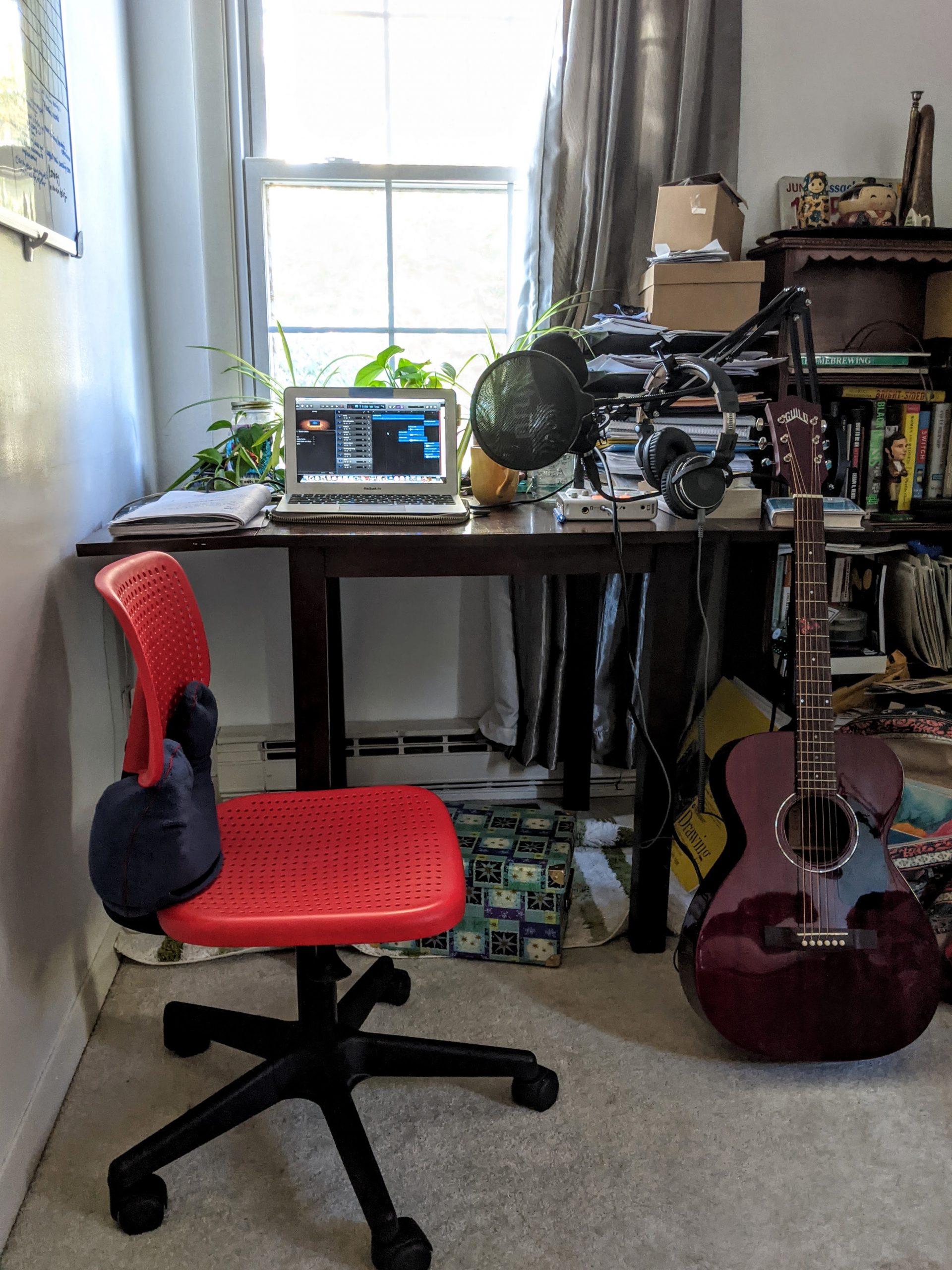 Brianna's office desk with a red chair, an acoustic guitar, and several plants