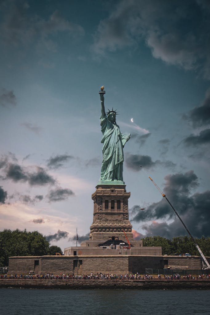 A view of the iconic Statue of Liberty on Liberty Island against a dramatic sky in New York City.